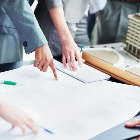 Groupe de professionnels en réunion analysant des plans et documents pour répondre à un appel d’offres BTP